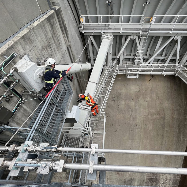 Looking down at three Rope Access workers installing an Electrical sensor on a Dam Spillway gate
