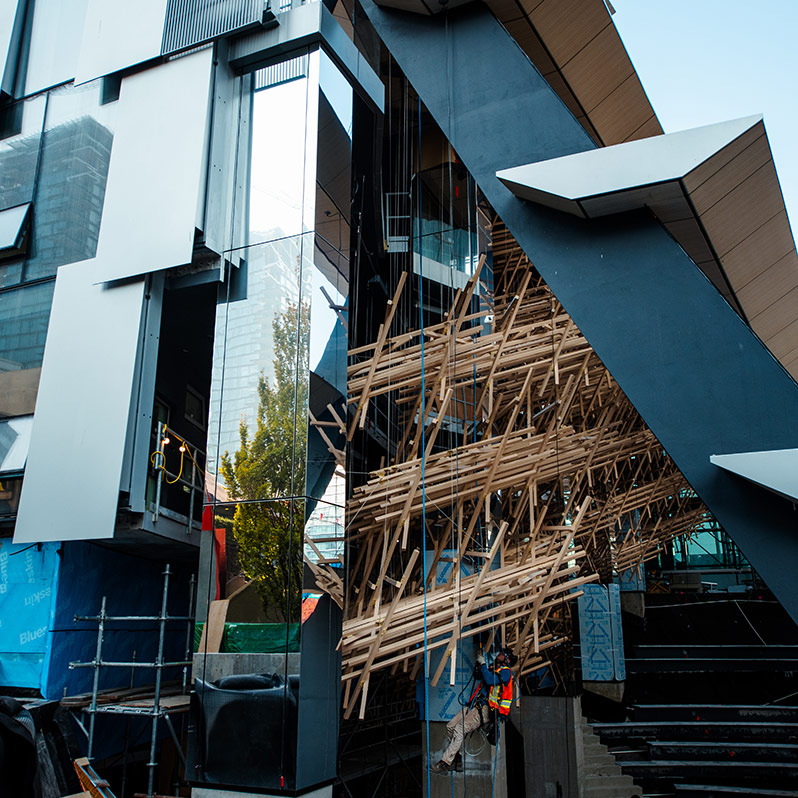 The Art sculpture by Kengo Kuma is seen through the side of the building above with rope access worker hanging below